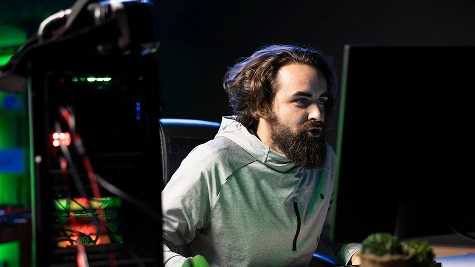 Een bebaarde mannelijke gamer die intensief op zijn computermonitor kijkt met een open-frame pc-behuizing en RGB-verlichting op de voorgrond.