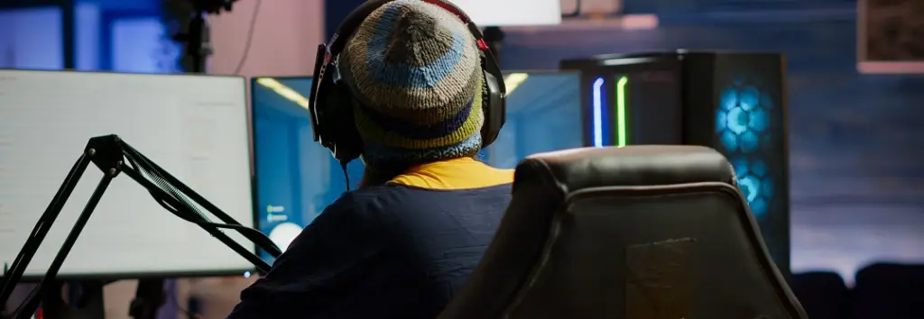 Een gamer met een muts en headset traint intensief voor een computerscherm tijdens een professionele coachingsessie.